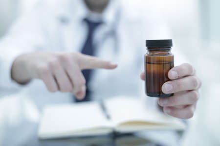 Doctor in a protective medical mask holds a jar of pills in his handの写真素材