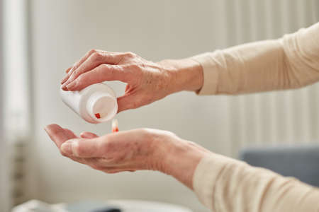 Senior woman sit on couch having daily vitamins or diet supplements at home, mature old female pensioner take dose of pills from meds bottle, elderly healthcare, medication conceptの写真素材