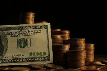 A large variety of coins and a hundred dollar bill on a black background. Stack of coins