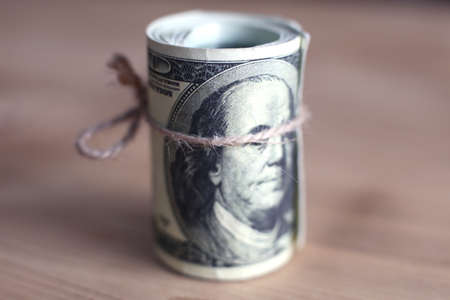 US dollars rolled up and tightened with band isolated on wood background