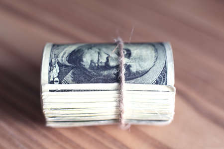 US dollars rolled up and tightened with band isolated on wood backgroundの写真素材
