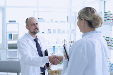 Pharmacists is Working. Man and Woman Handshaking with Each Other .. People Wearing Special Medical Uniform. People Located in Pharmacy.の写真素材