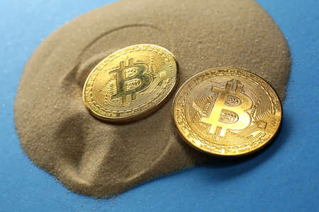 Two bitcoin coins on the sand on a blue backgroundの写真素材