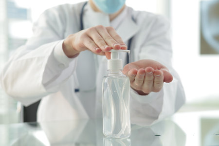 Doctor with a medical stethoscope in a protective mask in a clinic treats his hands with an antiseptic. Close-upの写真素材