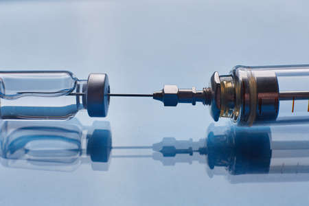 Glass vaccine vial and glass syringe on blue glass background