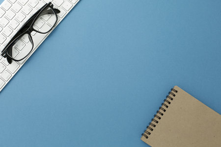 Glasses notpad and keyboard on blue background. Close-upの写真素材