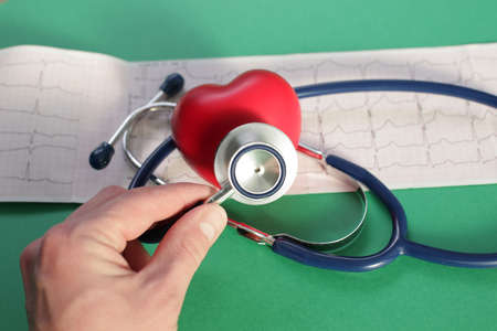 Doctors hand with medical stethoscope heart and cardiogram on green backgroundの写真素材