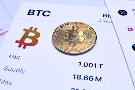 Coin of bitcoin cryptocurrency and chart of changes in cryptocurrency rates lie on a wooden table in the officeの写真素材