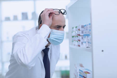 Man pharmacist in protective face mask working in drugstoreの写真素材