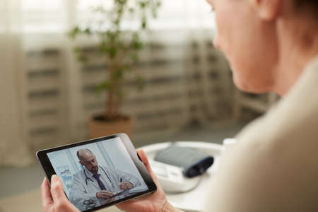 Telemedicine concept. Old woman with tablet during an online consultation with her doctor in her living roomの写真素材