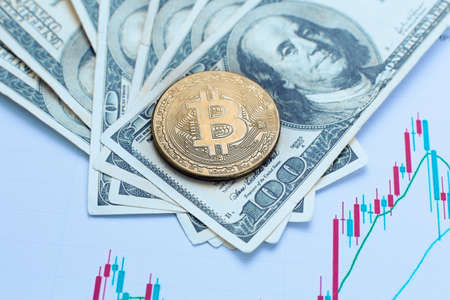 Bitcoin cryptocurrency coin lies on one hundred dollar bills and charts of cryptocurrency rate changesの写真素材