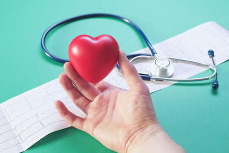 Doctors hand with medical stethoscope heart and cardiogram on green backgroundの写真素材