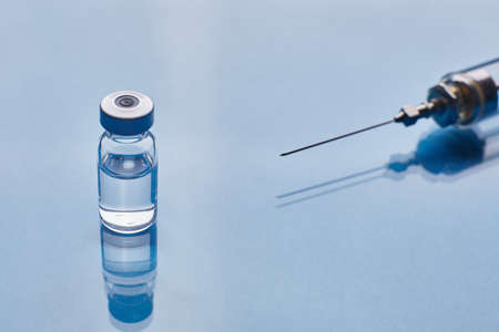 Glass vaccine vial and glass medical syringe on blue glass background