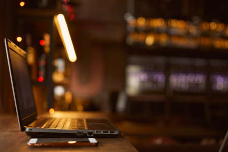 Laptop and mobile phone lie on a wooden table indoors in a cafe