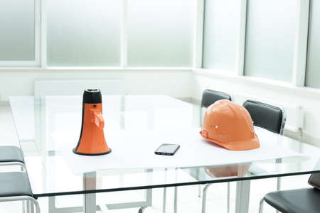 Loudspeaker construction hard hat on glass table in office spaceの写真素材