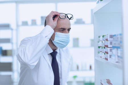 Man pharmacist in protective face mask working in pharmacyの写真素材