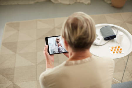 Telemedicine concept from home. Old woman with tablet during an online consultation with her doctor in her living roomの写真素材