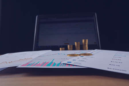 Two bitcoins are on the graphs of cryptocurrency rate changes on a laptop. In the background, several rows of coins and a laptop screen.の写真素材