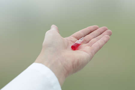A glass vial of red medicine is in the doctor's handの写真素材