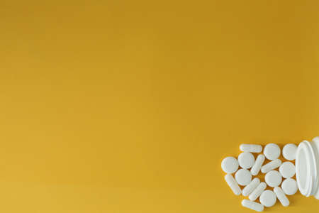On a yellow background lies a plastic bottle with medical pills scattered nearbyの写真素材