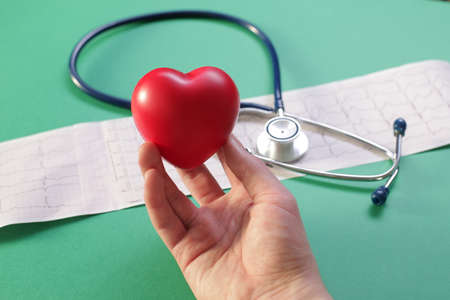 Doctors hand with medical stethoscope heart and cardiogram on green backgroundの写真素材