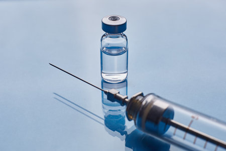 Glass vaccine vial and glass medical syringe on blue glass backgroundの写真素材