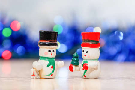 Merry christmas and happy new year greeting card. Close-up of snowmans in hats with a gift in their hands standing in soft-focus in the background. Christmas decorationsの写真素材