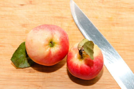 Red garden apple with leaf on cutting board with knife in soft-focus in the background, closeup. Delicious sweet and juicy fruits for salad cooking or bakery for background or wallpaperの写真素材