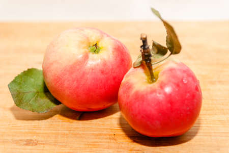 Red garden apple with leaf on cutting board on wooden table in soft-focus in the background, closeup. Delicious sweet and juicy fruits for salad cooking or bakery for background or wallpaperの写真素材