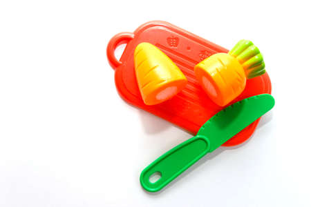 childrens plastic toy. plastic carrot on red cutting board with green knife isolated on white background in soft-focus in the backgroundの写真素材