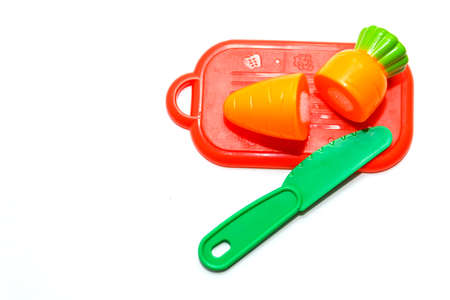 childrens plastic toy. plastic carrot on red cutting board with green knife isolated on white background in soft-focus in the background.の写真素材