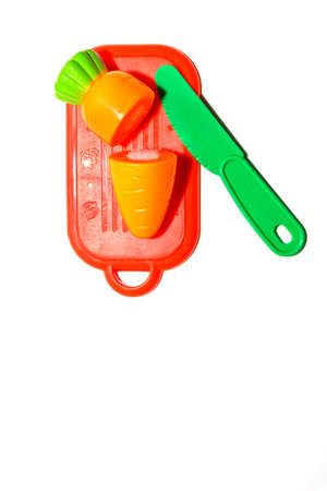 childrens plastic toy. plastic carrot on red cutting board with green knife isolated on white background in soft-focus in the background.の写真素材