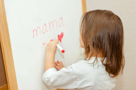 Girl writes Mama with marker on a blackboard. Mothers Day. I love my mom. girl draws heartsの写真素材