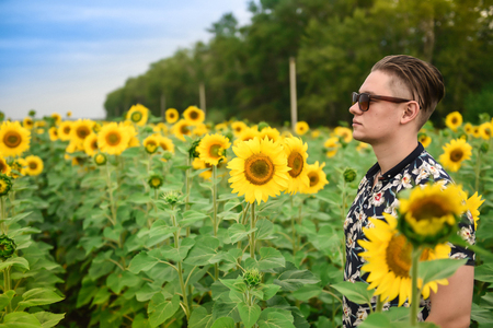 Man in a sunflower field. man is standing in a sunflower field with a blue sky background. Travaling and nature concept.の写真素材