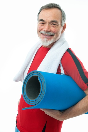 Senior man with a towel around neck holds a gym mat - isolated over white の写真素材