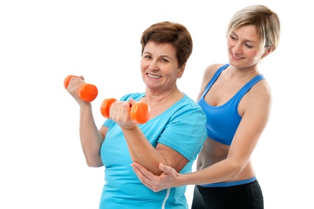 Senior woman doing fitness exercise with help of trainer at sport gymの写真素材