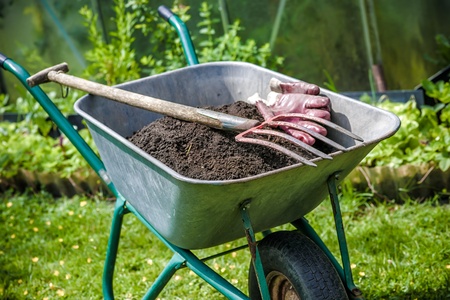 Pitch fork and gardening gloves in wheelbarrow full of humus soilの写真素材