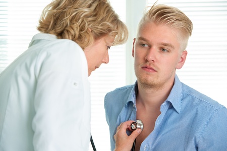 female doctor examining a young man in her officeの写真素材
