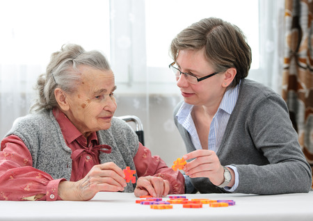 Elder care nurse playing jigsaw puzzle with senior woman in nursing home