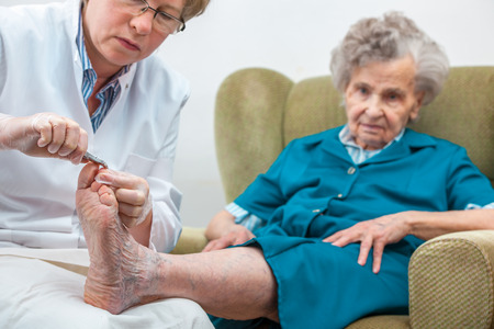 Nurse assists an elderly woman with chiropody and body care at homeの写真素材