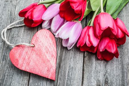 Bouquet of tulips with an empty tag and red heart on wooden backgroundの写真素材