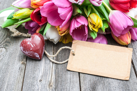 Bouquet of tulips with an empty tag and red heart on wooden backgroundの写真素材