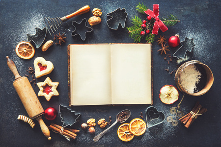 Christmas baking sweet food frame with recipes book, homemade cookies, spices, kitchen utensils, fir branches and red holiday decoration on dark rustic baking tray. Top viewの写真素材