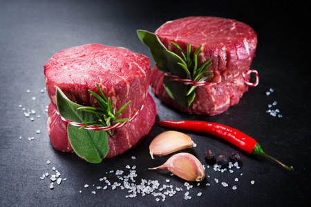 Raw beef fillet steaks mignon with spices on dark backgroundの写真素材
