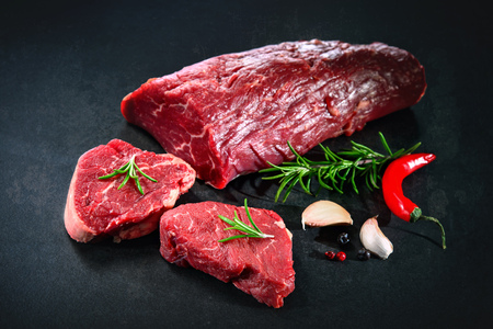 Fresh and raw beef meat. Whole piece of tenderloin with steaks and spices ready to cook on dark backgroundの写真素材