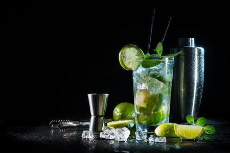 Mojito cocktail with fresh mint, lime, ice cubes and bar shaker on dark backgroundの写真素材
