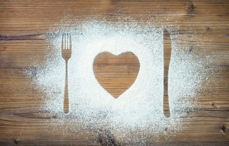 Fork, knife and plate in heart shape, flour sprinkled around the wooden boardの写真素材