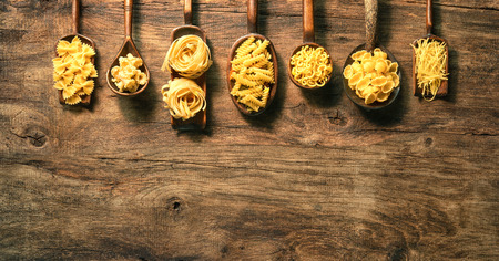 Various pasta on spoons over wooden background. Top view with copy spaceの写真素材