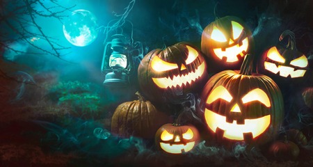 Halloween pumpkin head jack lantern with burning candles in scary deep night forest