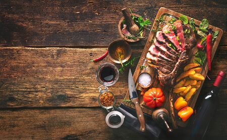 Grilled meat, sliced tomahawk beef steak with spices, french fries and vegetables on a rustic backgroundの写真素材
